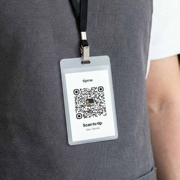 Barista wearing a name badge on a lanyard, printed with a tipme QR code and "Scan to tip"