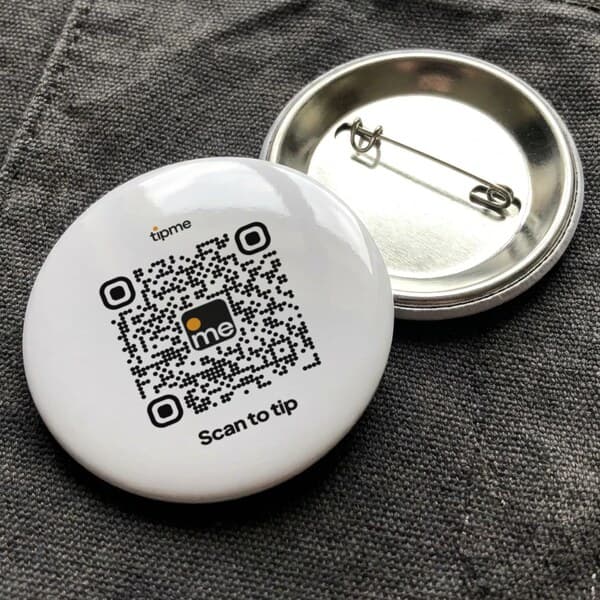Round pin badge printed with a tipme QR code, next to a second badge turned over to show its safety pin