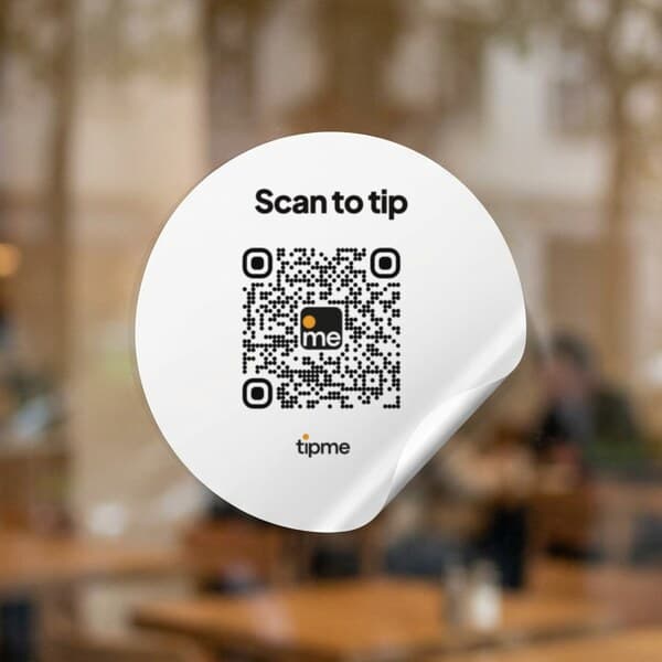Round tipme QR code sticker on a cafรฉ glass door, one edge peeling up