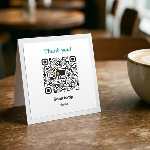 Tent card reading "Thank you!" with a tipme QR code, on a cafรฉ table next to a latte